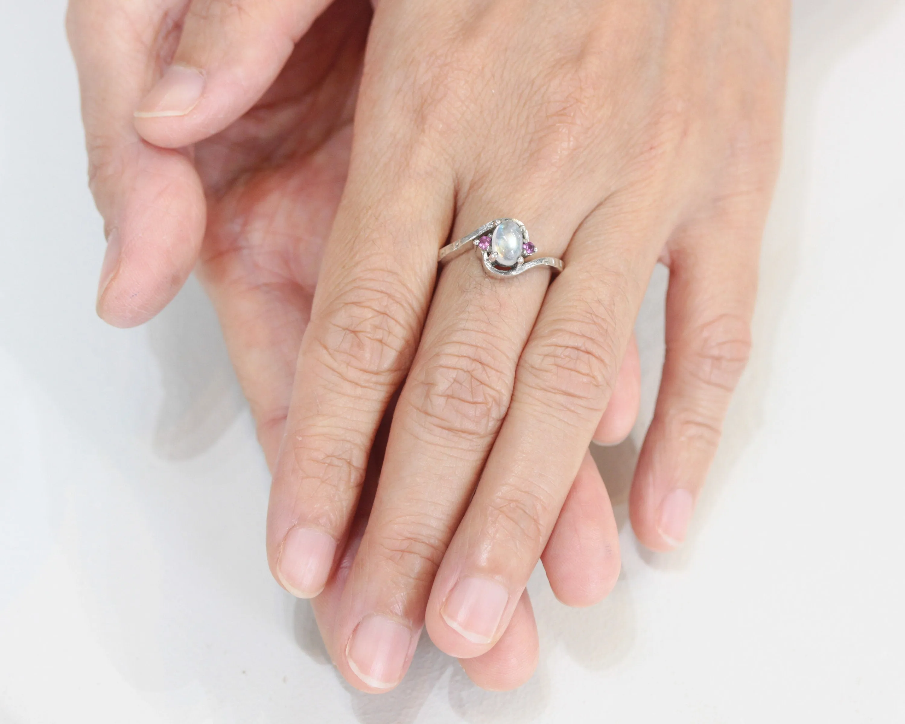 Oval cabochon moonstone ring with pink sapphire side set gems in prongs setting with sterling silver oxidized texture band