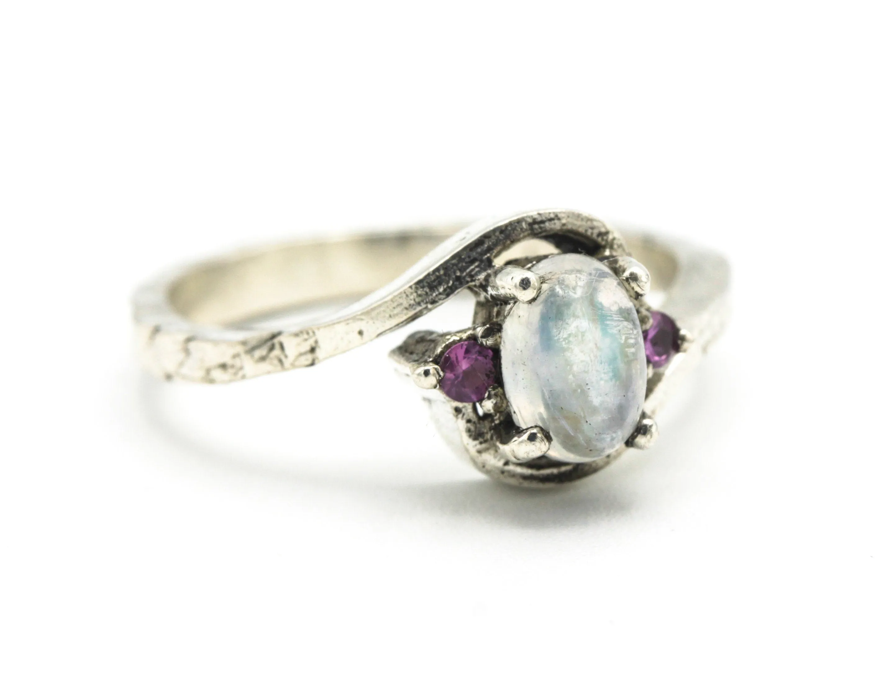 Oval cabochon moonstone ring with pink sapphire side set gems in prongs setting with sterling silver oxidized texture band