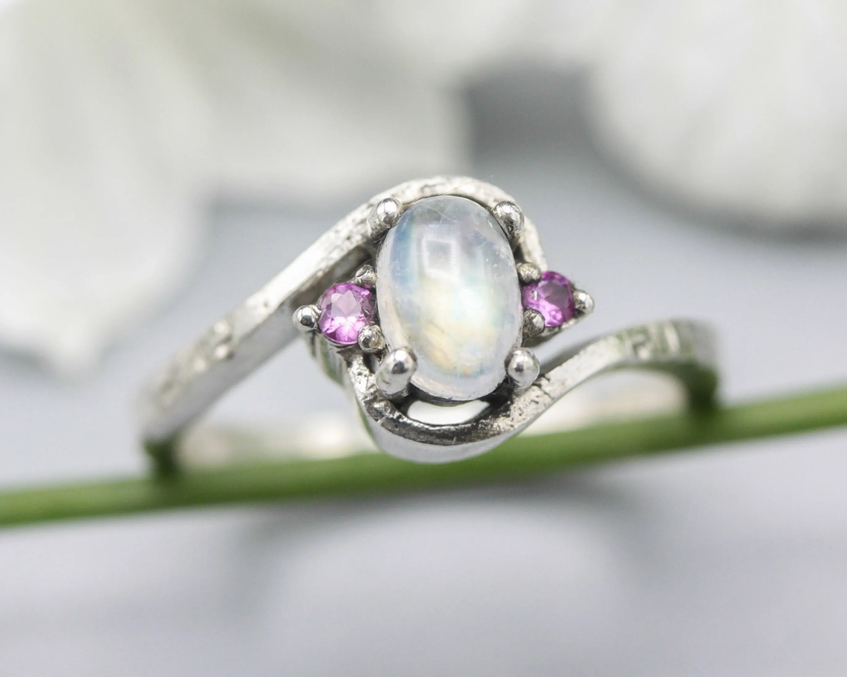 Oval cabochon moonstone ring with pink sapphire side set gems in prongs setting with sterling silver oxidized texture band